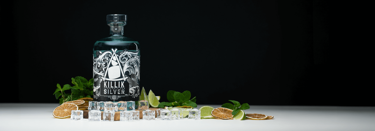 Killik Silver gin bottle with botanicals on a white surface against a black background