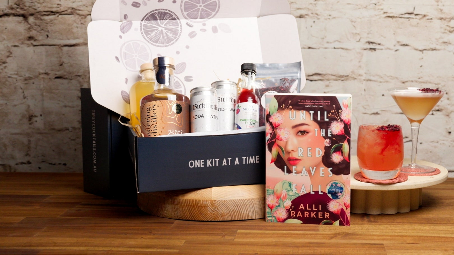 Gifting set with a book, drinks, and decorative items on a wooden surface.