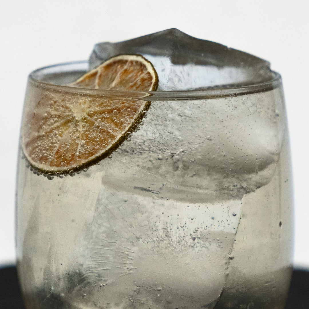 Glass of gin & Tonic with a lime wedge and ice cube on a white background
