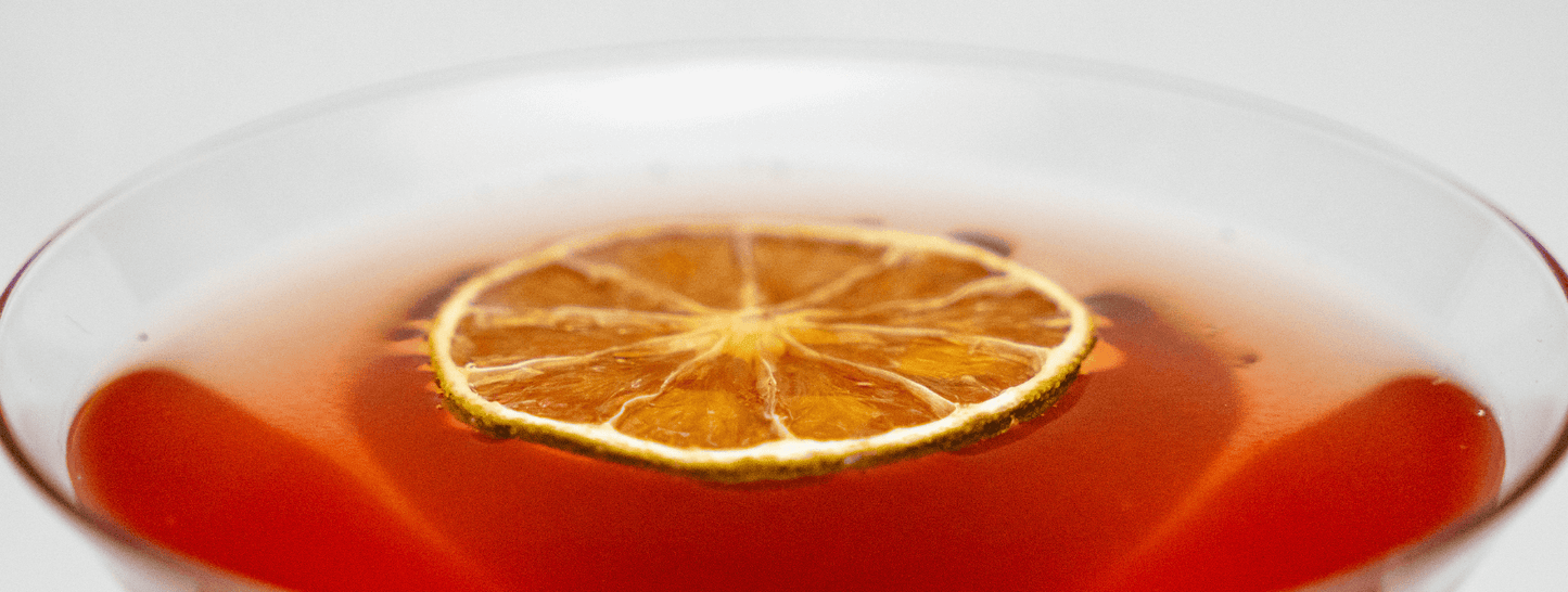 Close up of top of martini glass with cosmopolitan cocktail inside garnished with a dried lime wheel on a white background