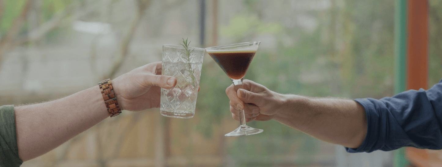 Two hands holding a cocktail each, meeting in the middle for a cheers with a blurred background.