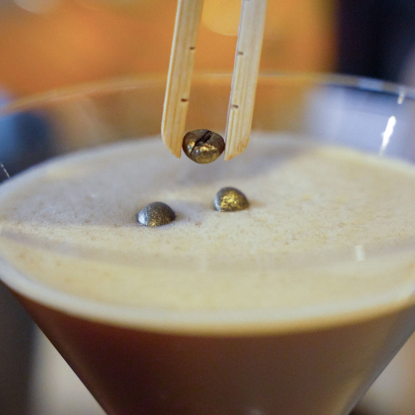 Close up of espresso martini showing person garnishing cocktail with three golden coated espresso beans 
