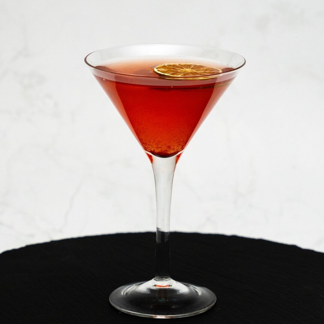 Pink Cosmopolitan cocktail in a martini glass with a lime wheel on a white background
