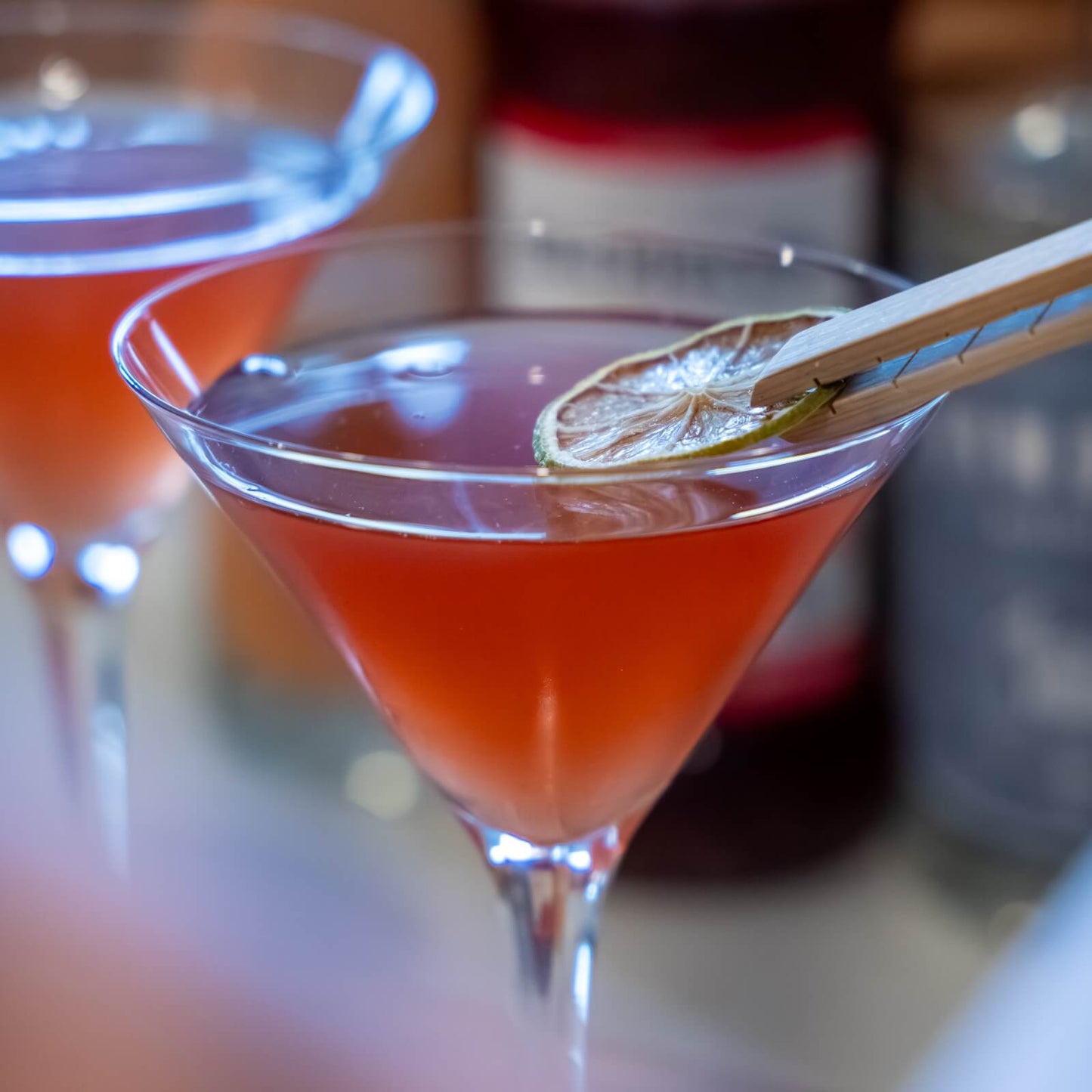 Pink cosmopolitan in a martini glass being garnished with dried lime with a blurred background