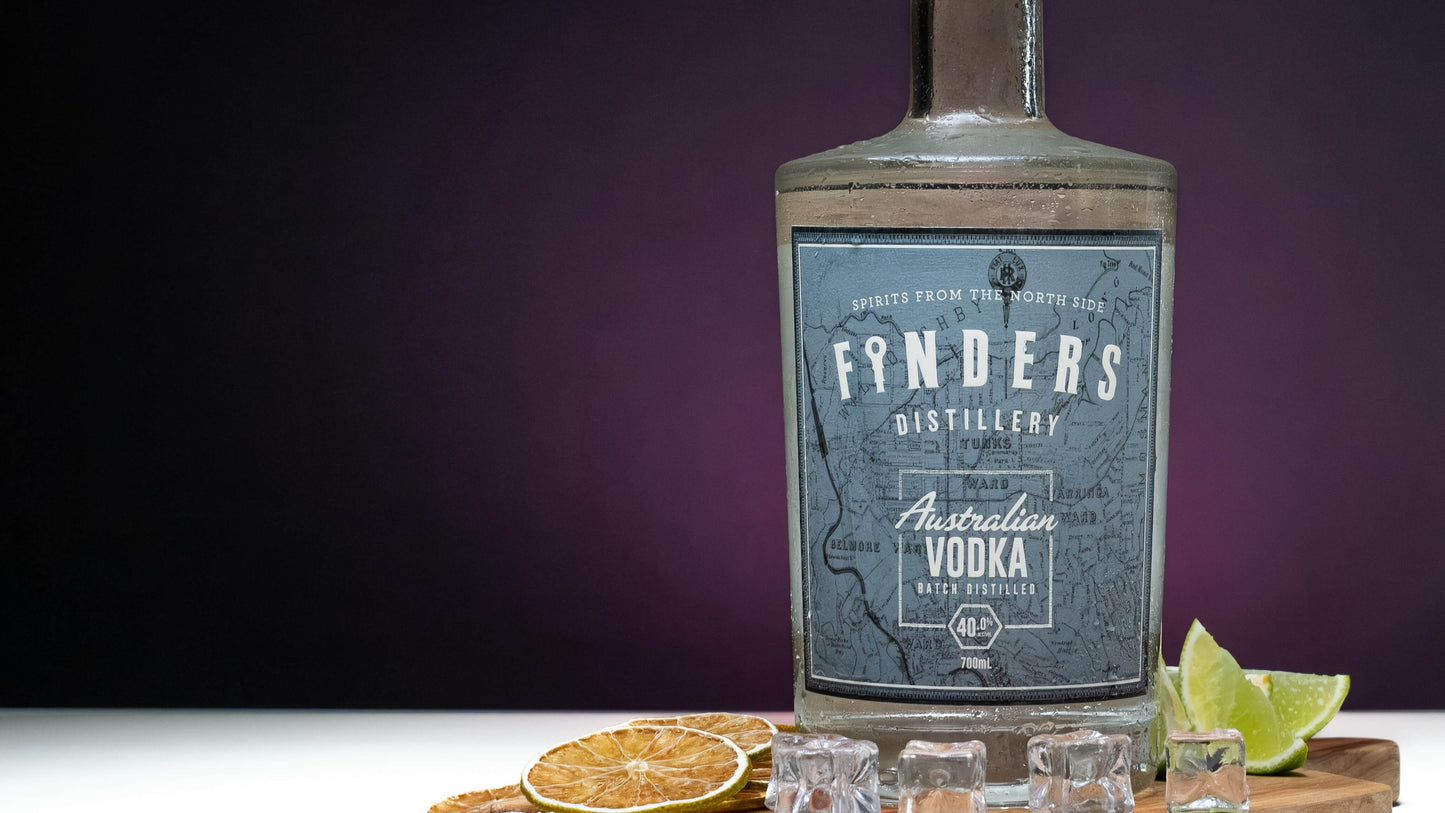 Finders Distillery Vodka on a wooden board with ice, fresh lime, dried lime slices and a purple hazed background