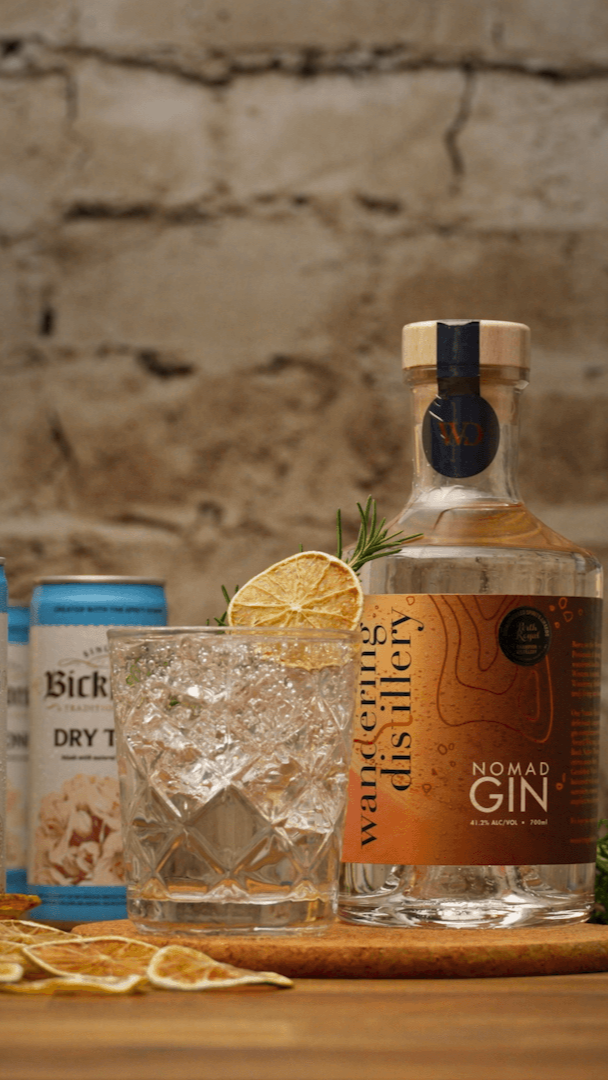 Cocktail kit showing cocktail with bottle of gin, elderflower syrup and other ingredients on wooden bench with stone background