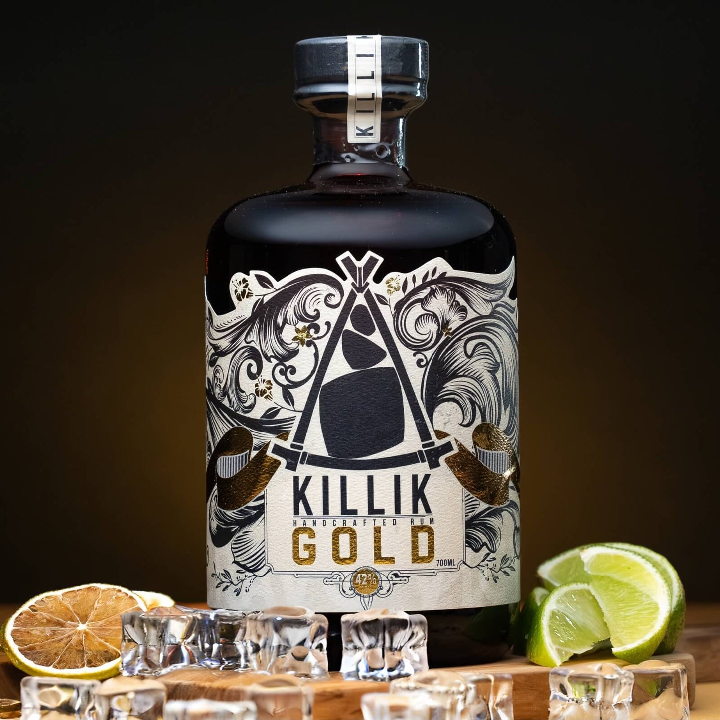 Bottle of Killik Gold Rum on a wooden board with ice, fresh limes and dried limes with a dark background