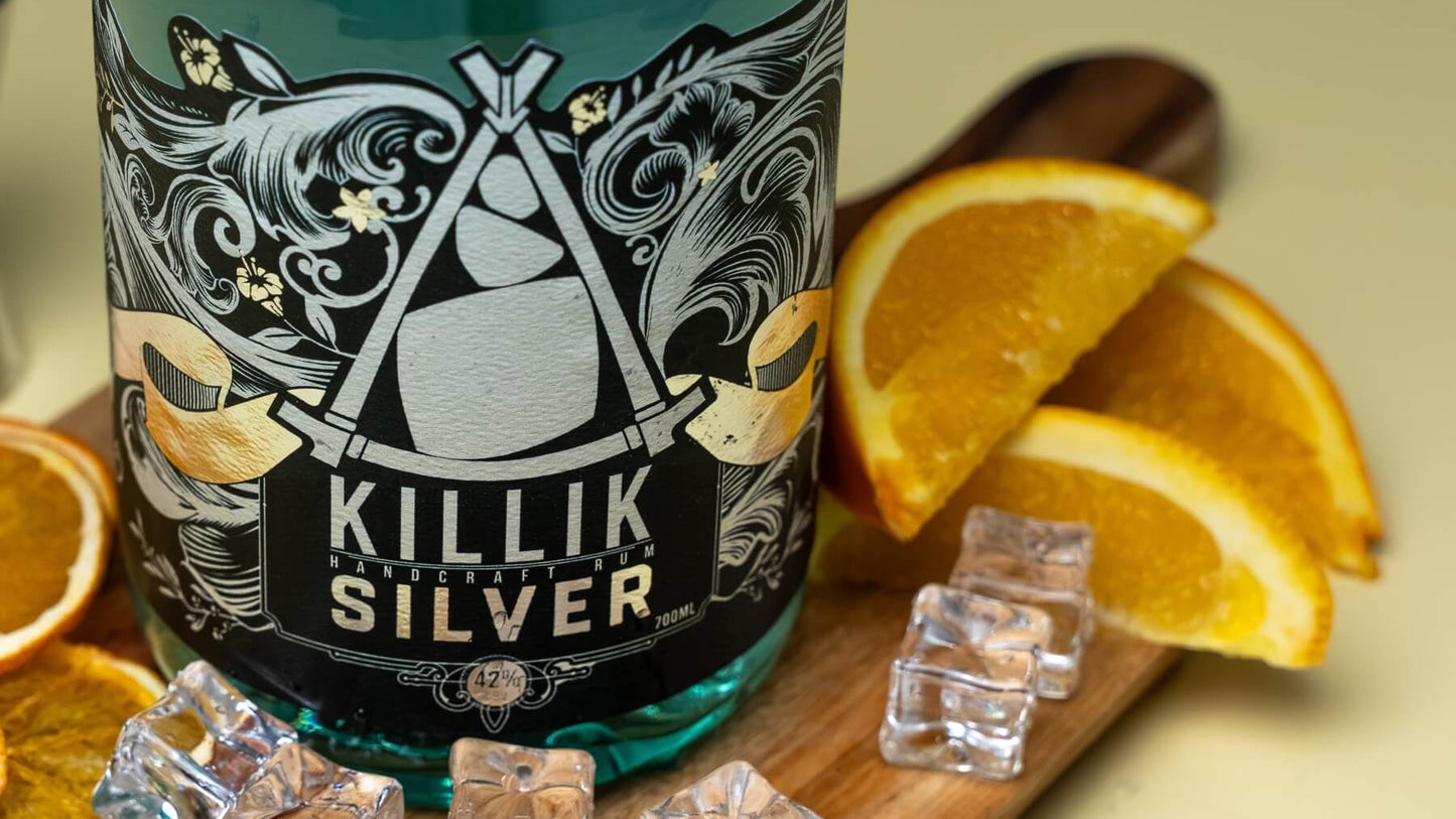 Close up of Killik Silver bottle on wooden board with fresh orange slices next to it and light yellow background