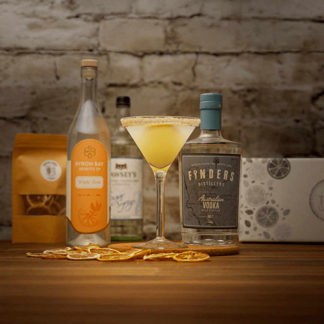 Bottles of alcohol such as finders distillery vodka and Byron Bay triple zest liqueur with a lemon drop martini cocktail on a wooden surface with a stone wall background