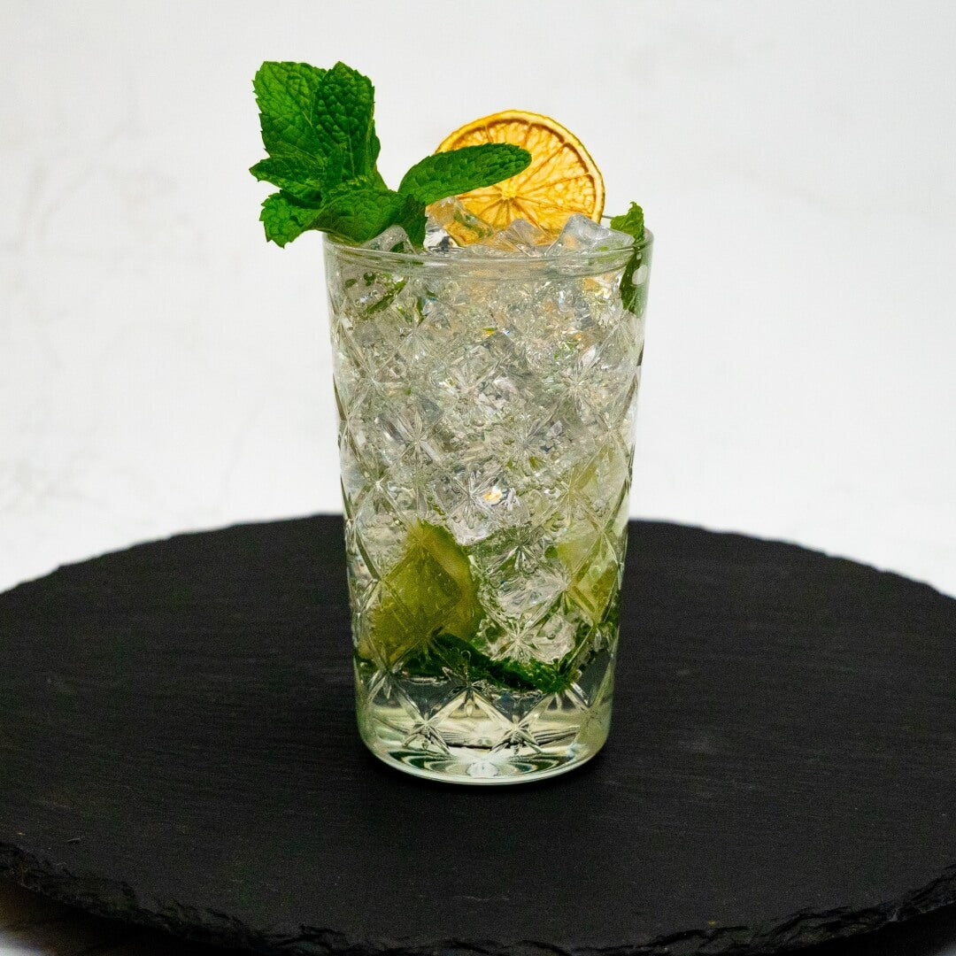 Mojito Cocktail with ice, lime slice, and mint leaf on a black slate surface.