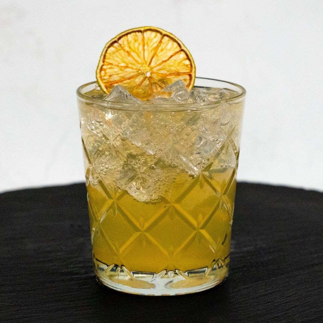 Glass of Moscow Mule cocktail with ice and a dried lime slice on a black surface.