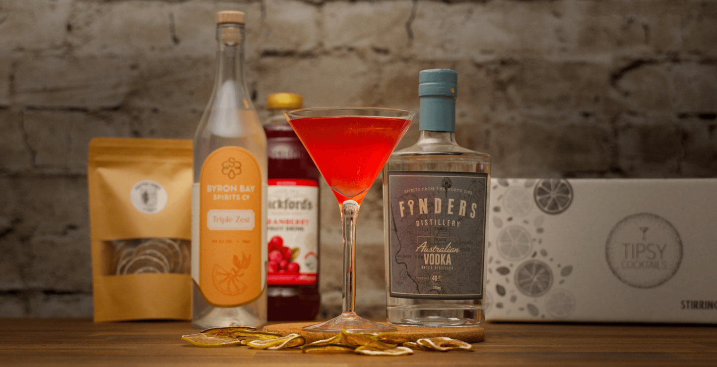 Beverage setup with bottles, a cocktail glass, and packaging on a wooden surface with a stone wall background.