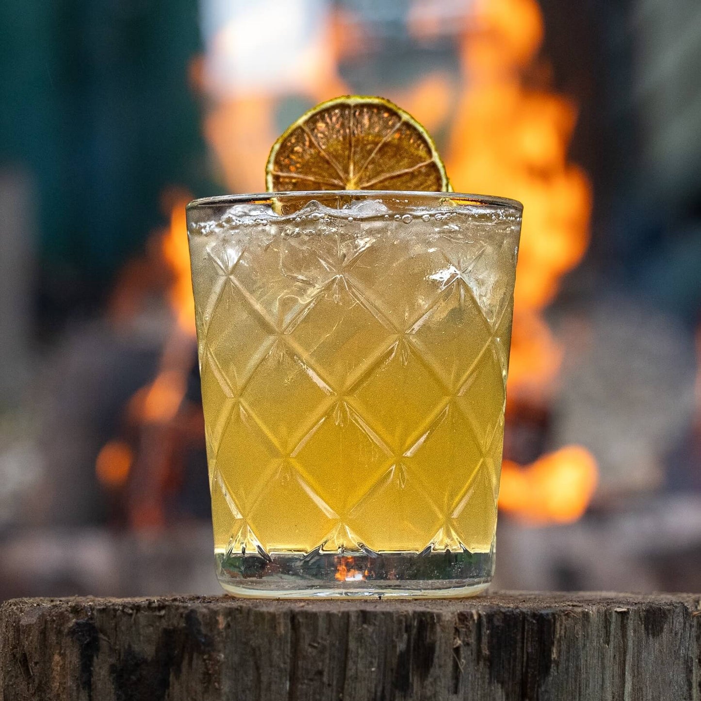 The forecast cocktail sitting on top of a wooden log with dried lime slice. Background blurred showing a winter fire 