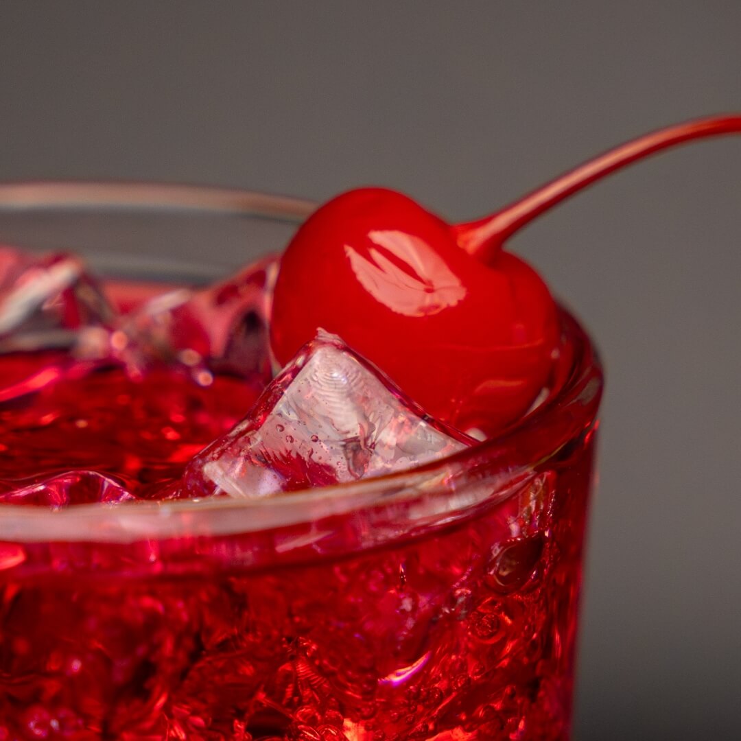 Red cocktail with a cherry on a grey background