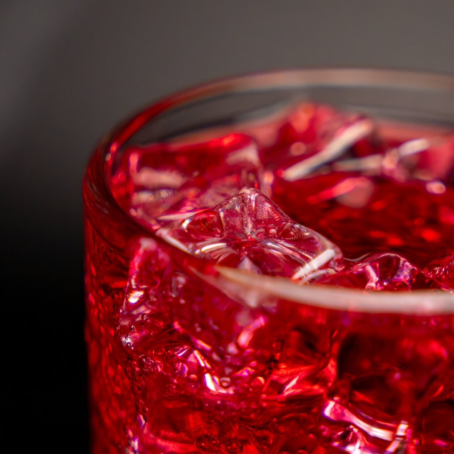 Close up of a glass with a red Shirley temple drink inside and ice blocks on the top of the drink, dark background 