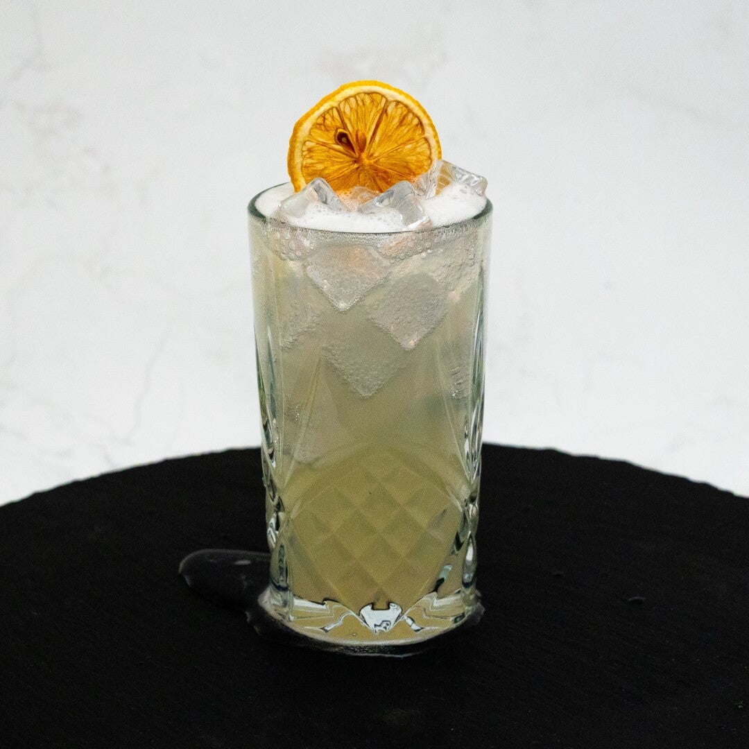 Summer Zest Cocktail with ice and a lemon slice in a glass on a black surface.