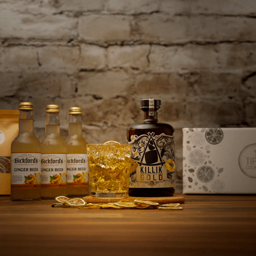 Bottle of Killik Gold with a glass of the forecast cocktail as amber liquid on a wooden surface against a stone wall background.