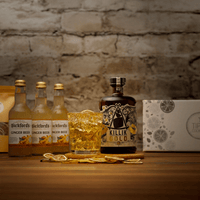 Bottle of Killik Gold with a glass of the forecast cocktail as amber liquid on a wooden surface against a stone wall background.