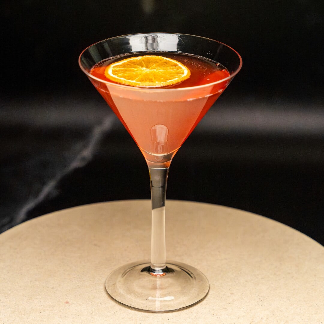 Pink mocktail with an orange slice in a martini glass on a dark background