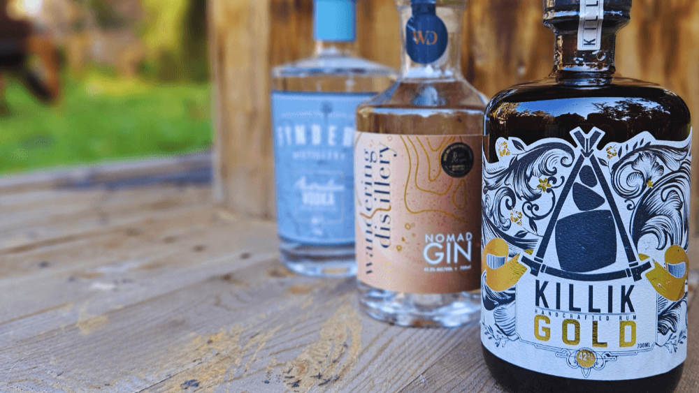 Three bottles of gin on a wooden surface with a blurred outdoor background