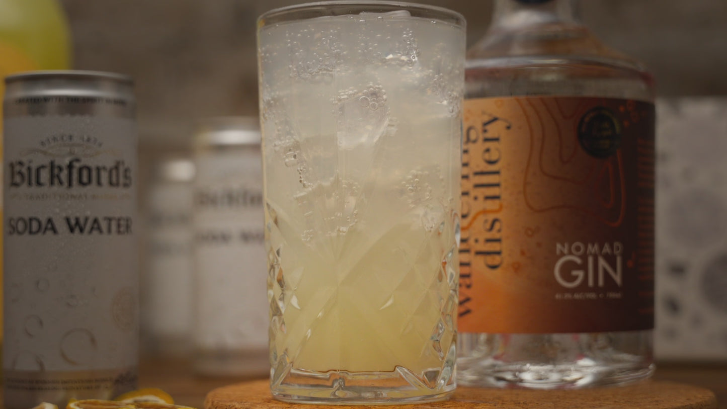 Video shows a close up of the summer zest cocktail in a tall glass, being garnished with a dried lemon slice. Video zooms out to show cocktail kit contents including a bottle of gin, soda water cans and dried lemon garnishes. Video reverses back in to close up of the cocktail.