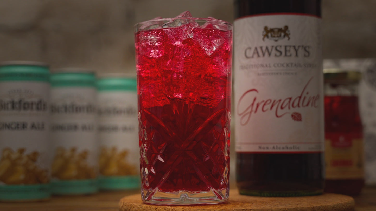 Video is of a red mocktail being garnished with a red cherry. Zooming out to see remainder of ingredients for the mocktail. Zooming back in to reverse the video effect on a wooden bench with stone background. 
