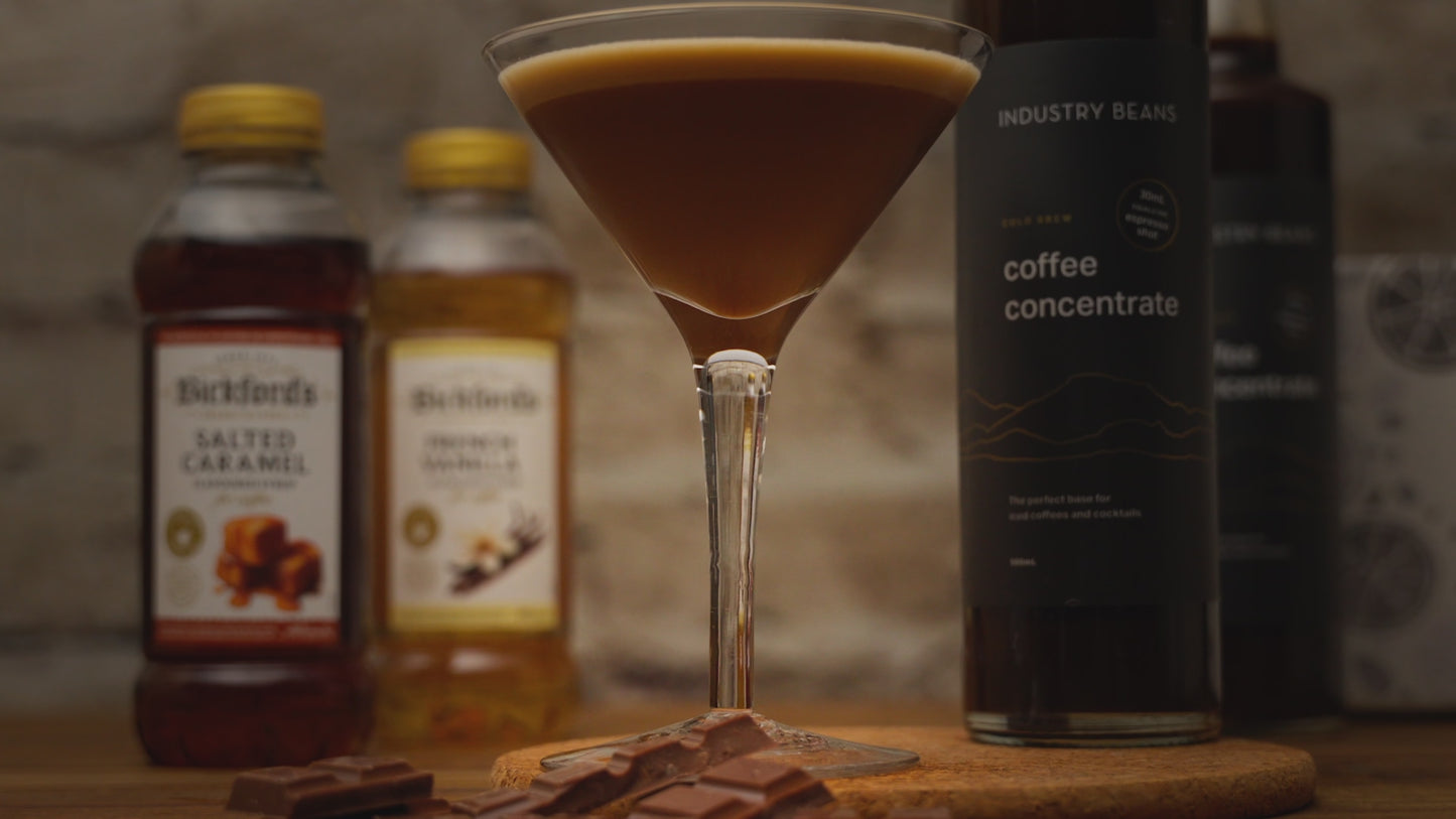 Video shows a close up of a coffee mocktail. Zooming out to see ingredients on a wooden table with stone background. Zooming back in to the close up of the mocktail