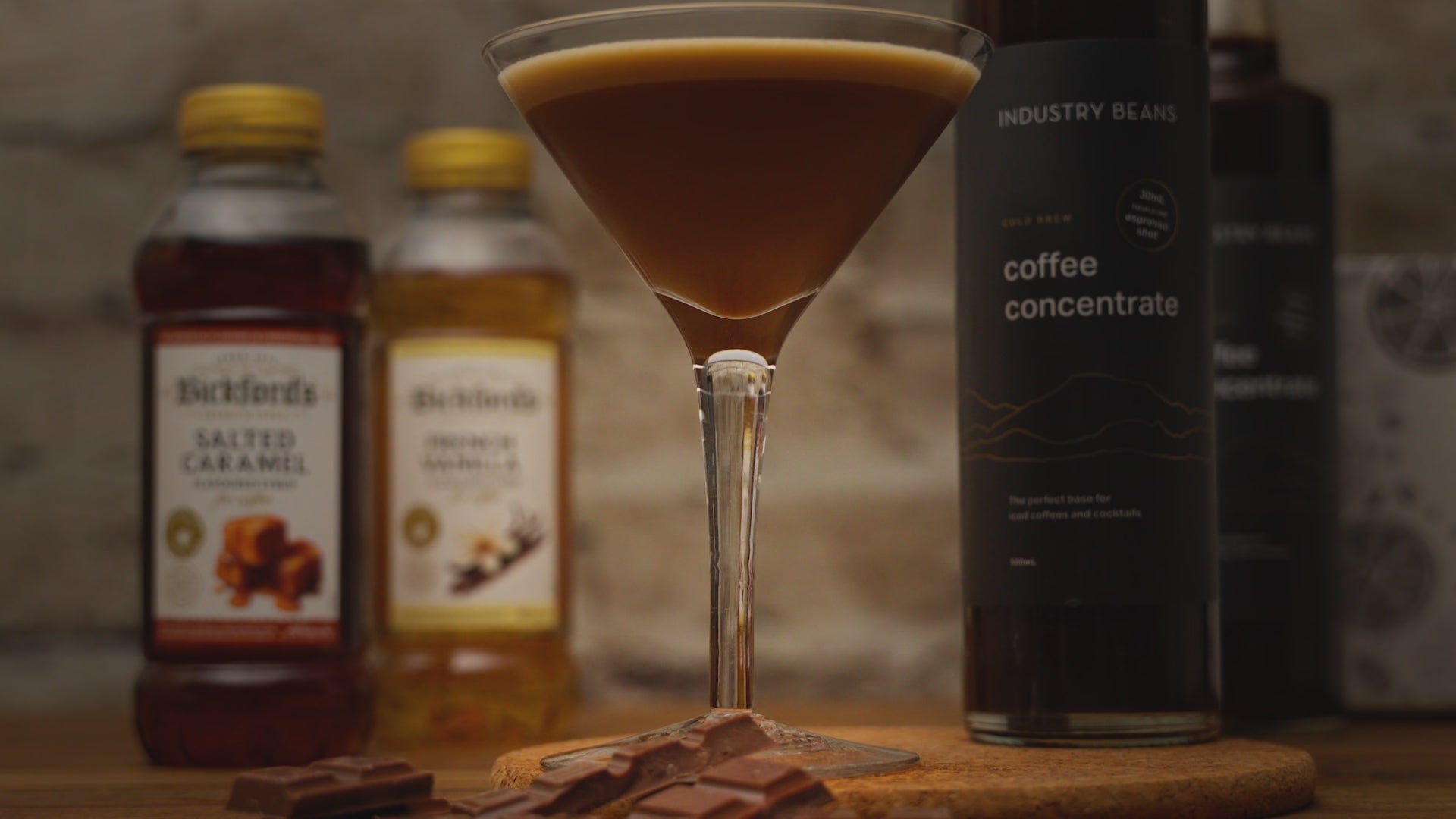 Video shows a close up of a coffee mocktail. Zooming out to see ingredients on a wooden table with stone background. Zooming back in to the close up of the mocktail