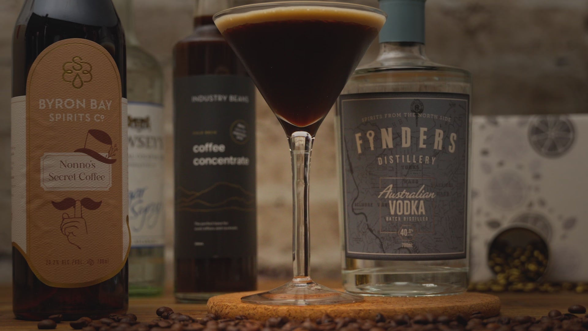 Video of the Espresso Martini Cocktail Kit. Espresso Martini Cocktail in tall martini glass with person garnishing drink with a coffee bean. Video zooms out to show kit contents including Finders Distillery Vodka, Byron Bay Spirit Co's Coffee Liqueur, Industry Beans Coffee Concentrate and sugar syrup with coffee beans surrounding items. Video reverses back in including a reverse of the drink being garnished. 